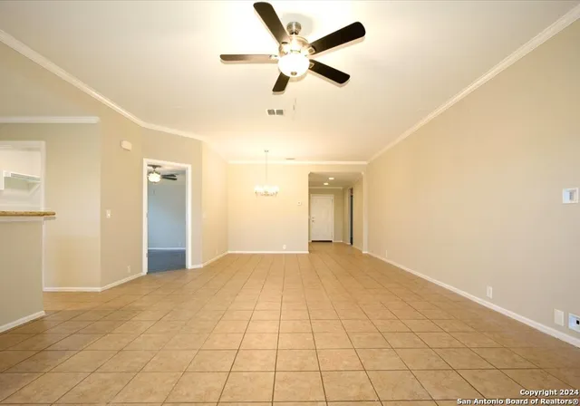 a view of an empty room and a ceiling fan & kitchen view