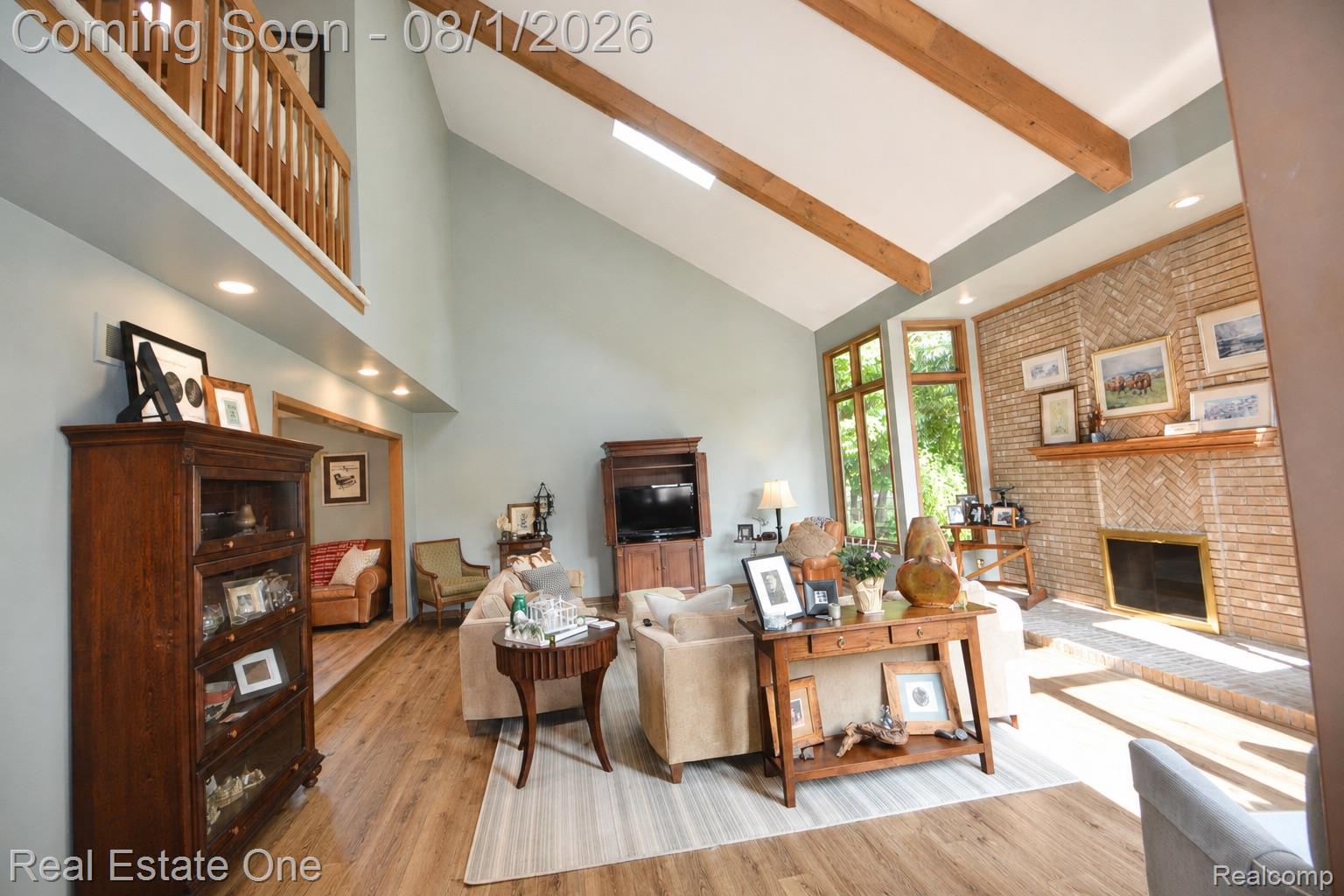 1370 Springwood Lane Rochester, MI 48309 - Photo 27 of 37 Vaulted ceiling living area featuring exposed wood beams, a brick fireplace with a wood mantle, large bay windows, wood-finish flooring, and a second-story open-rail balcony