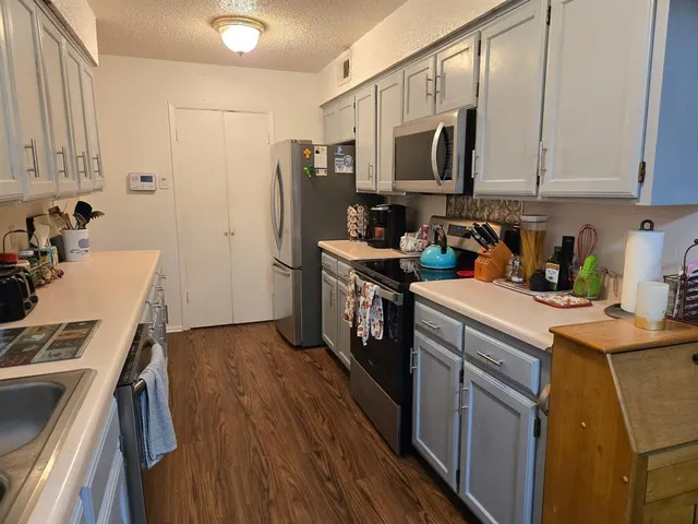 a kitchen with stainless steel appliances a stove top oven a sink a refrigerator white cabinets and wooden floor