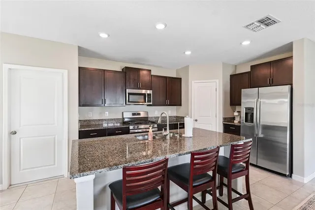a kitchen with stainless steel appliances granite countertop a refrigerator a stove a sink a dining table and chairs