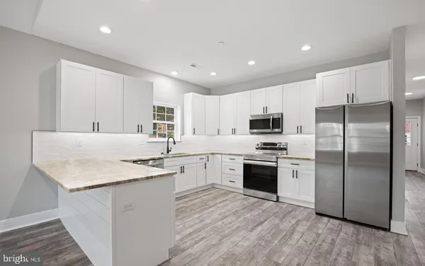 a kitchen with stainless steel appliances granite countertop a refrigerator a sink dishwasher a stove and white countertops with wooden floor
