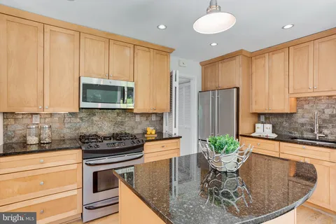 a kitchen with stainless steel appliances granite countertop a stove a sink a microwave a dining table and chairs with white cabinets