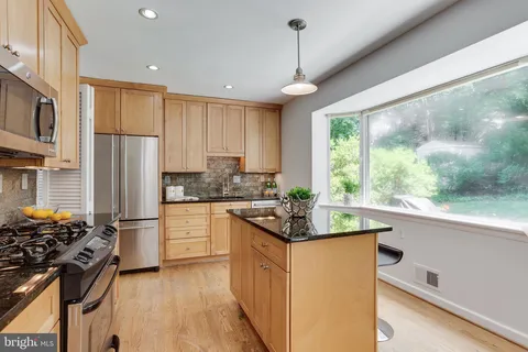 a kitchen with stainless steel appliances granite countertop a refrigerator a sink dishwasher a stove and white countertops with wooden floor