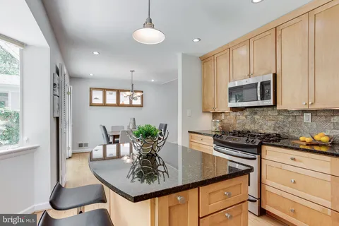 a kitchen with stainless steel appliances granite countertop a sink a stove a dining table and chairs with wooden floor