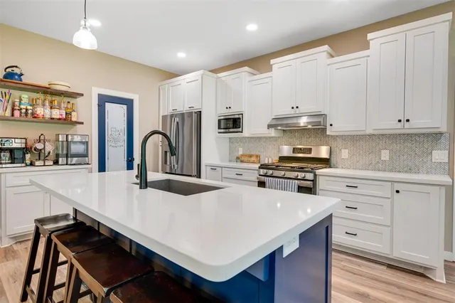 a kitchen with kitchen island stainless steel appliances a sink a stove and a wooden floors