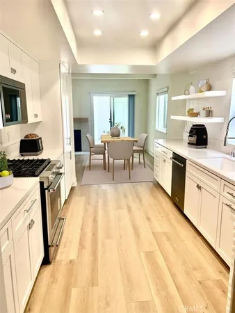 a open kitchen with stainless steel appliances granite countertop a stove top oven a sink dishwasher and white cabinets with wooden floor