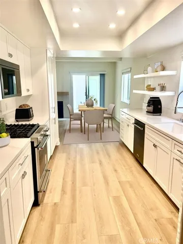 a open kitchen with stainless steel appliances granite countertop a stove top oven a sink dishwasher and white cabinets with wooden floor