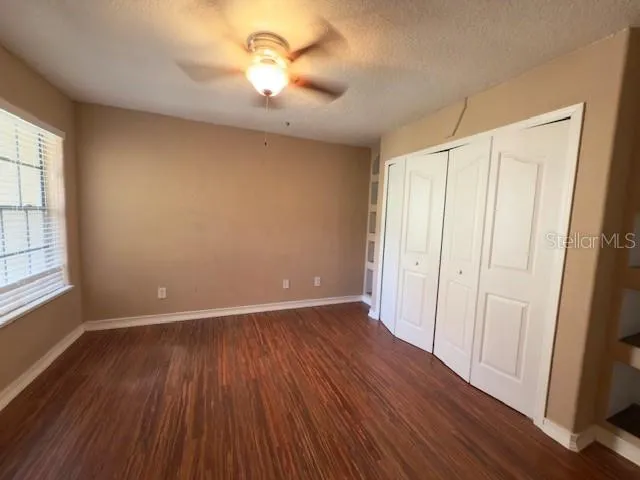 an empty room with wooden floor chandelier fan and windows