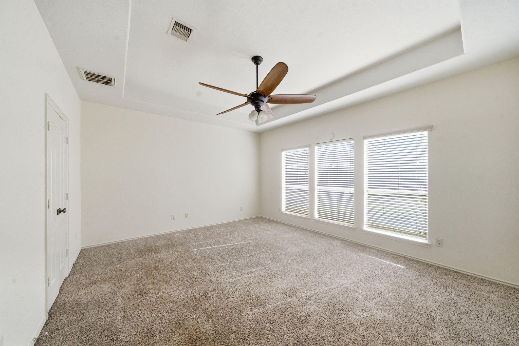 23139 Tranquil Spring Lane Katy, TX 77494 - Photo 12 of 22 Primary Bedroom is a spacious room featuring soft carpet flooring, large windows with blinds for ample natural light, and a ceiling fan for comfort. The neutral walls and tray ceiling add elegance, while the double-door entry enhances accessibility.