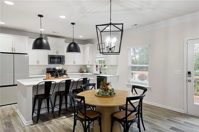 a kitchen with stainless steel appliances a dining table chairs a refrigerator and cabinets
