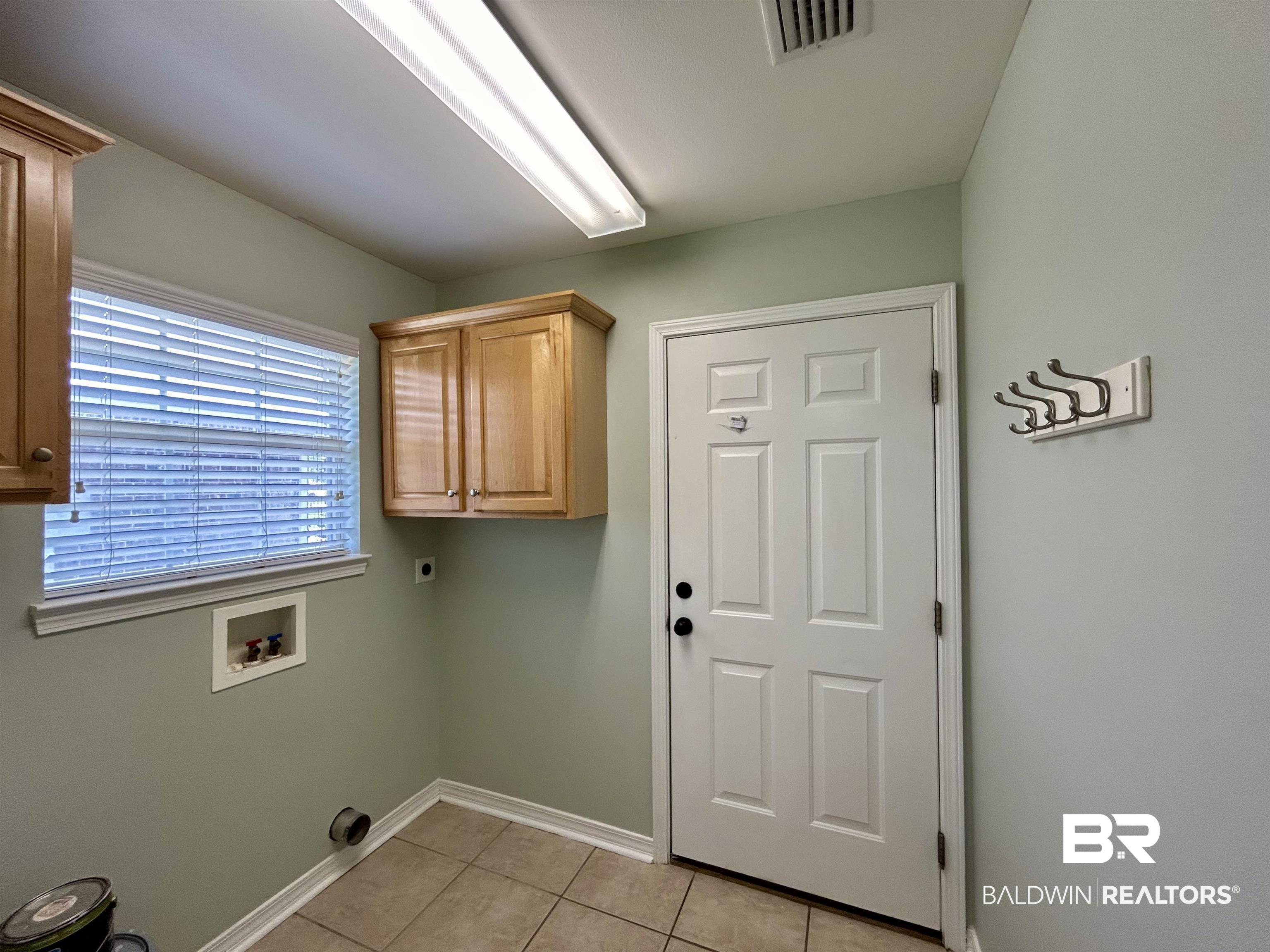 7198 Raintree Lane Gulf Shores, AL 36542 - Photo 26 of 33 Utility room featuring a window with blinds, upper wood cabinetry, a paneled door, and tile flooring