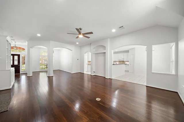 a view of an empty room with wooden floor and a kitchen