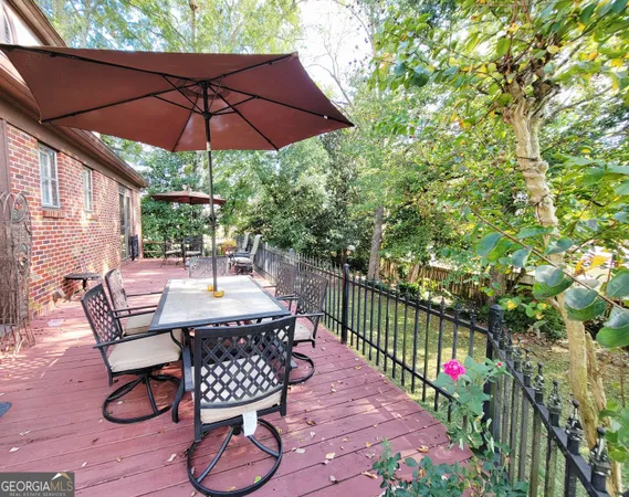 a view of a patio with table and chairs under an umbrella with large trees