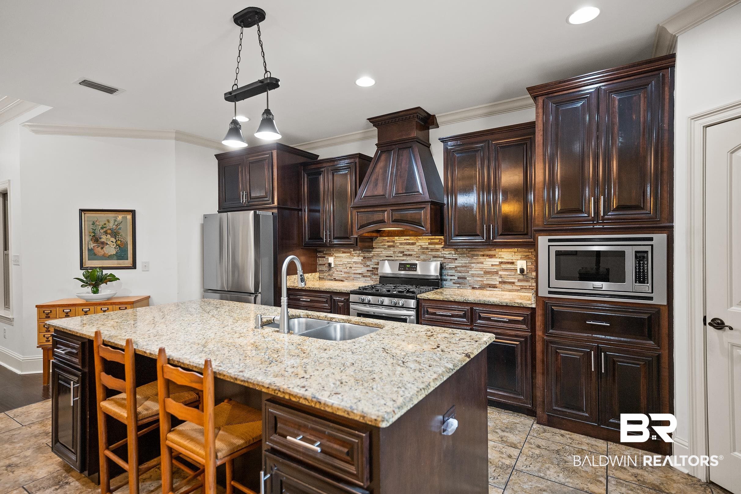 313 Pecan Ridge Boulevard Fairhope, AL 36532 - Photo 7 of 51 Spacious kitchen featuring an expansive center island with an undermount sink, granite countertops, dark wood cabinetry, stainless steel appliances, and a tiled backsplash