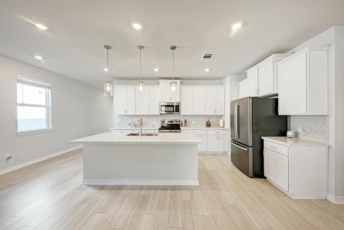 113 Rampart Loop Liberty Hill, TX 78642 - Photo 6 of 40 a kitchen with stainless steel appliances granite countertop a refrigerator a sink dishwasher a oven and white cabinets with wooden floor