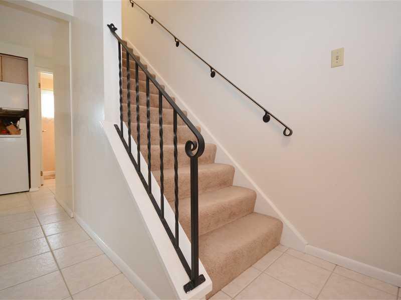 Entry/Foyer. The foyer has ceramic tile flooring, as well as a guest coat closet (not shown). The carpeted stairs lead to the upper level. The living room is to the left of the foyer. A glimpse into the kitchen and powder room is offered at the top left.