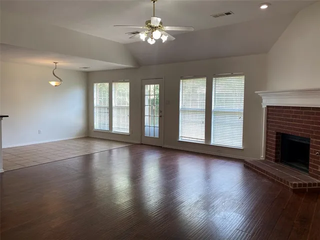 an empty room with wooden floor fireplace and windows