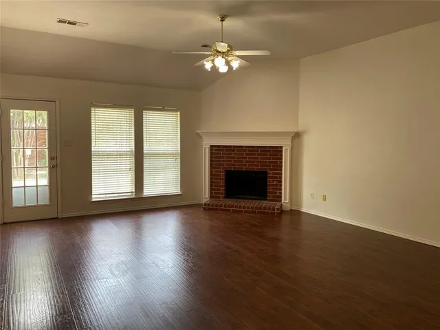 an empty room with wooden floor fireplace and windows