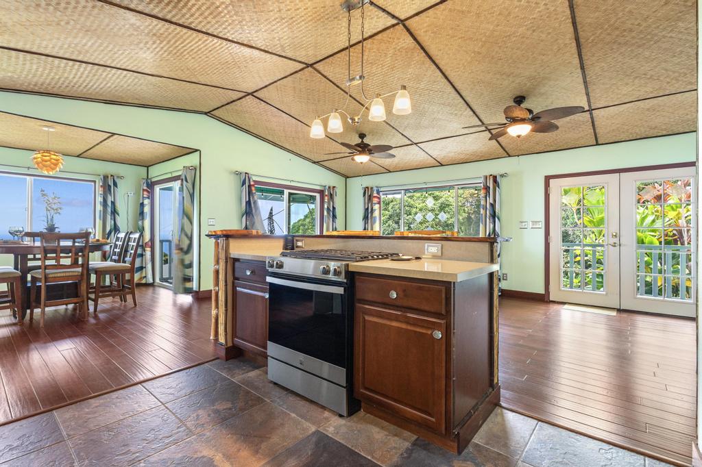 87-2707 Hawaii Belt Road Captain Cook, HI 96704 - Photo 12 of 30 a kitchen with stainless steel appliances granite countertop a stove a refrigerator a couch and a dining table with wooden floor