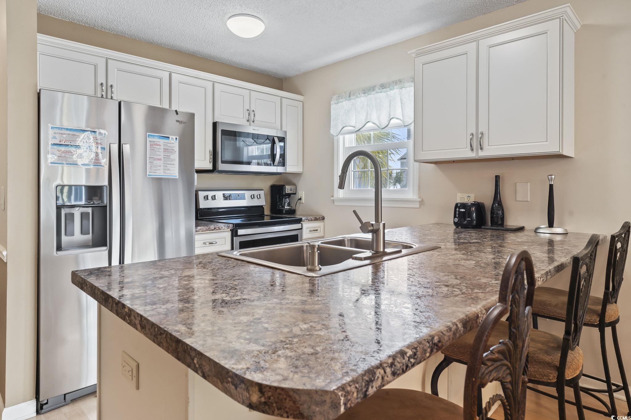 1425 North Waccamaw Drive, Unit 123 Murrells Inlet, SC 29576 - Photo 4 of 39 Kitchen with appliances with stainless steel finishes, a peninsula, a textured ceiling, a breakfast bar area, and white cabinets