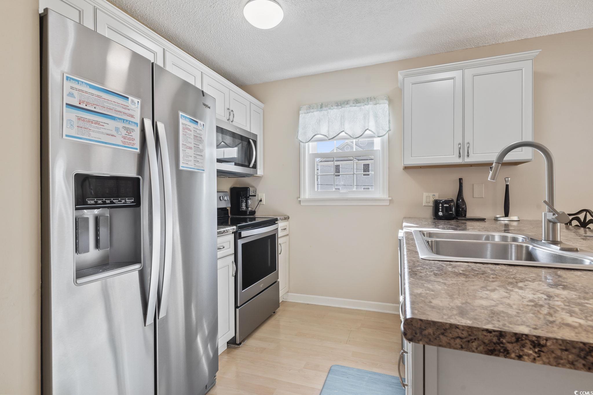 1425 North Waccamaw Drive, Unit 123 Murrells Inlet, SC 29576 - Photo 5 of 39 Kitchen featuring appliances with stainless steel finishes, white cabinetry, light wood finished floors, and a textured ceiling