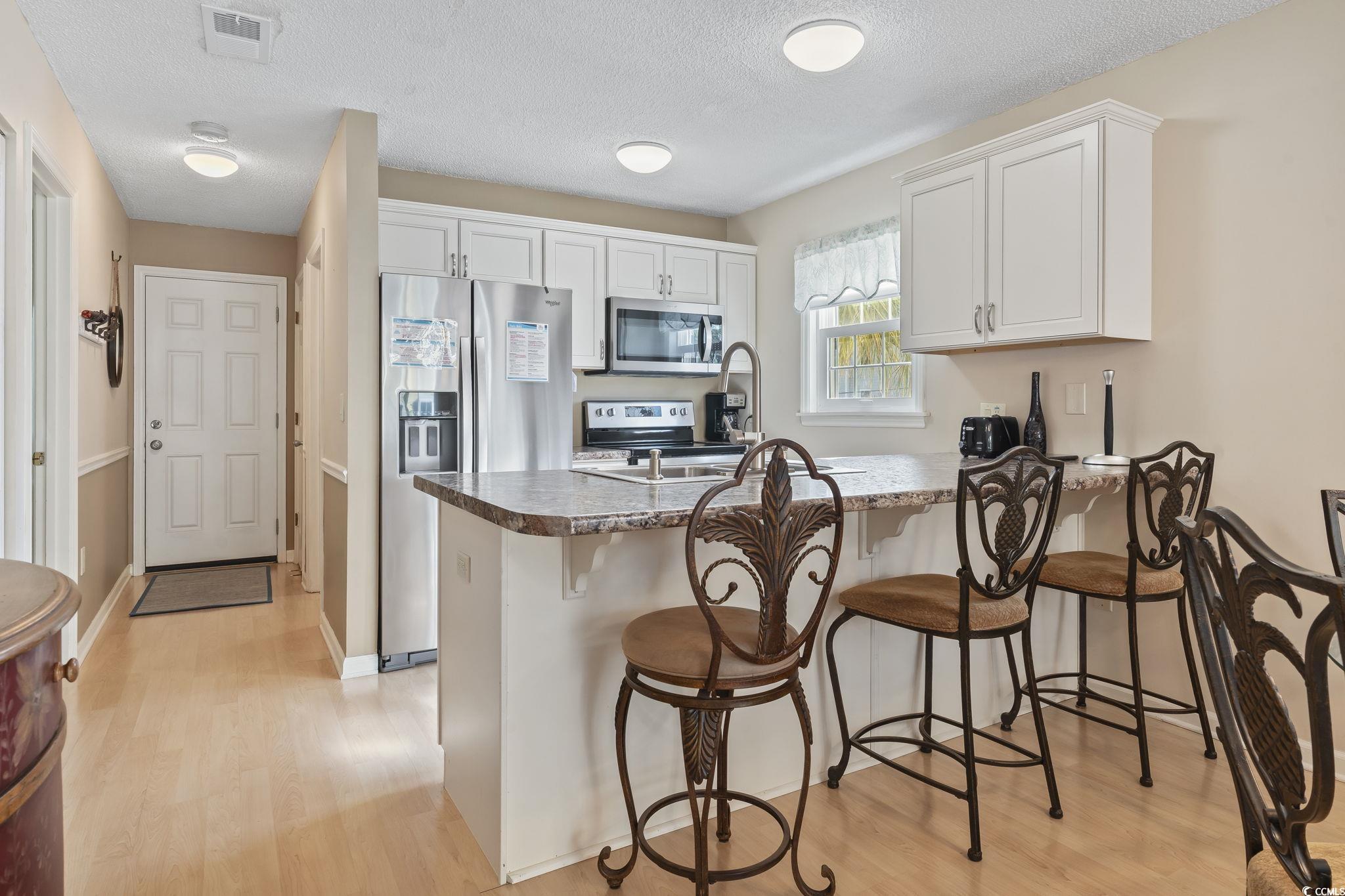 1425 North Waccamaw Drive, Unit 123 Murrells Inlet, SC 29576 - Photo 7 of 39 Kitchen featuring a peninsula, appliances with stainless steel finishes, light wood-type flooring, a textured ceiling, and a kitchen breakfast bar