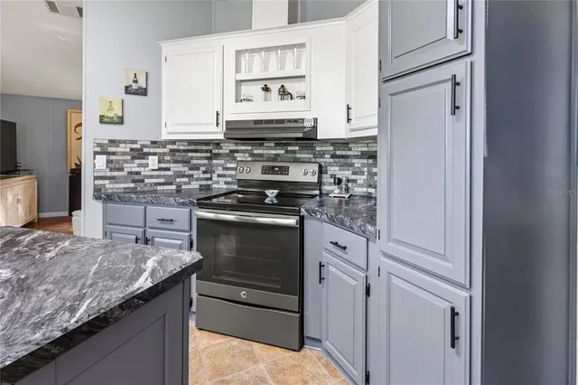 a kitchen with stainless steel appliances granite countertop a stove a sink and a dining table with white cabinets