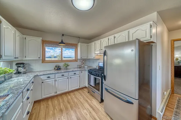 a kitchen with stainless steel appliances granite countertop a refrigerator a sink dishwasher a stove and white countertops with wooden floor