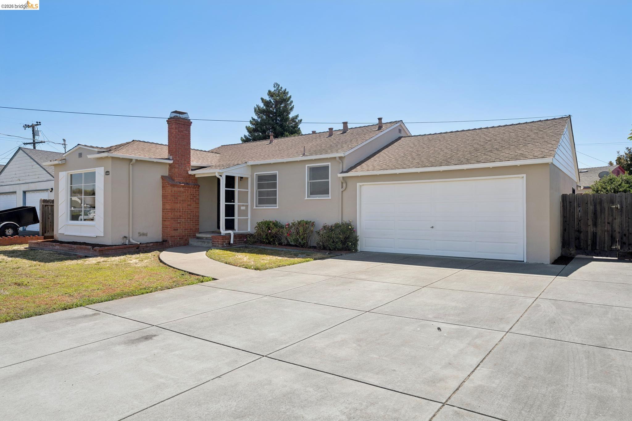 15162 Inverness Street San Leandro, CA 94579 - Photo 2 of 25 Single-story residence featuring a two-car garage with a white overhead door, a brick chimney, and a bay window