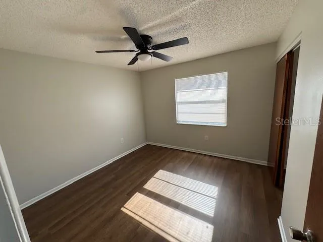 an empty room with wooden floor fan and windows