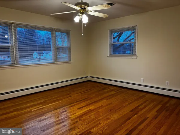 a view of an empty room with wooden floor and a chandelier fan