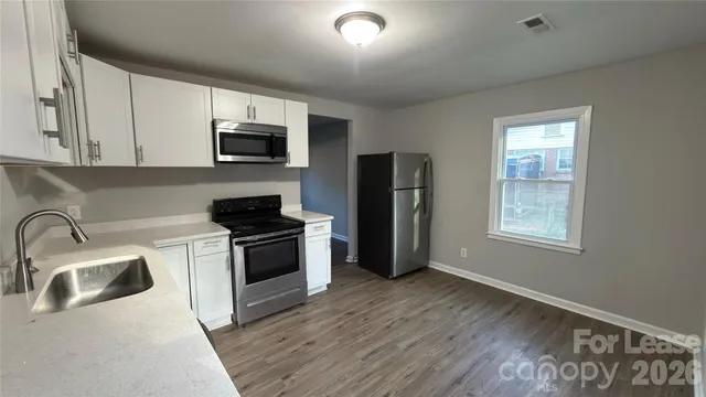 a kitchen with stainless steel appliances a sink a stove a microwave a refrigerator a sink and dishwasher with wooden floor