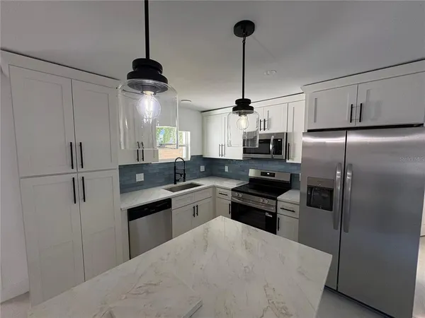 a kitchen with stainless steel appliances granite countertop a refrigerator a sink a stove and white cabinets
