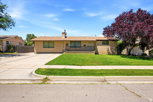7050 South 260 East Midvale, UT 84047 - Photo 2 of 28 Traditional ranch-style home featuring a brick and siding exterior, a covered front porch with black railing, a paved driveway, and a mature tree providing shade