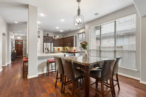 a dining room with stainless steel appliances kitchen island granite countertop a dining table chairs and wooden floor