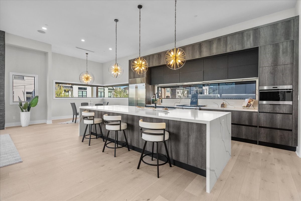 516 Reinerman Street Houston, TX 77007 - Photo 11 of 42 This modern kitchen features a sleek design with an expansive island, stylish pendant lighting, and ample counter space. High-end appliances are integrated into dark cabinetry, and large windows provide plenty of natural light.