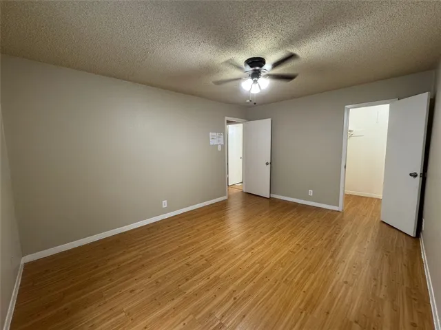 a view of an empty room with wooden floor and a ceiling fan