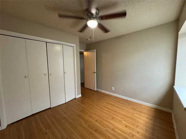 an empty room with wooden floor fan and windows