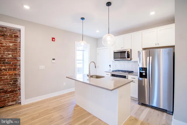 a kitchen with stainless steel appliances granite countertop a refrigerator a sink dishwasher a stove and a wooden floor