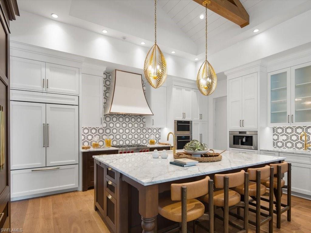 620 Binnacle Drive Naples, FL 34103 - Photo 7 of 49 Kitchen featuring an island with sink, light stone countertops, decorative backsplash, premium range hood, and white cabinetry