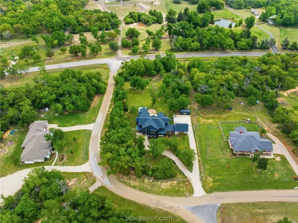 an aerial view of a house with yard and trees in the background
