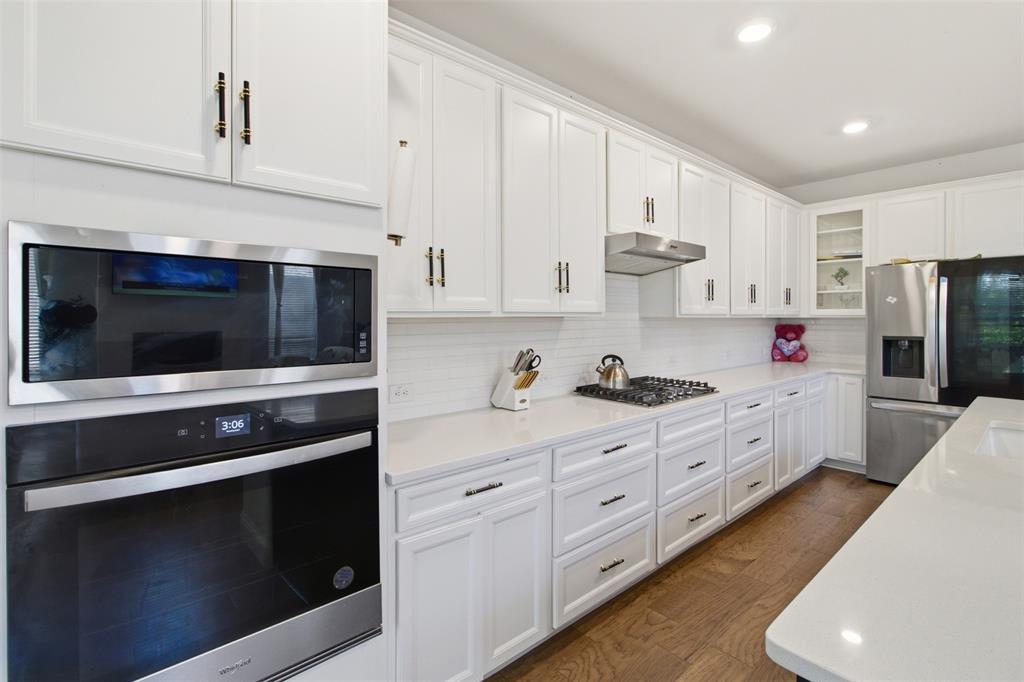 7416 Sequoia Rdg Road Little Elm, TX 76227 - Photo 19 of 37 Contemporary kitchen featuring white cabinetry, quartz countertops, a tile backsplash, stainless steel appliances, and wood-finish flooring