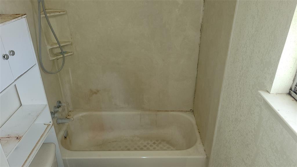 902 South Old Temple Road Hewitt, TX 76643 - Photo 19 of 32 White bathtub with a shower head and built-in shelving, complemented by a window with a white sill