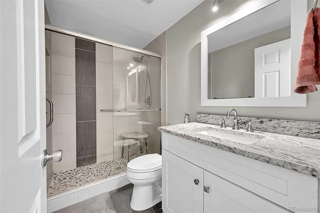 a bathroom with a granite countertop sink toilet a mirror a vanity and shower