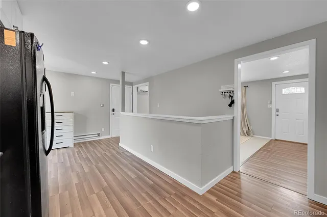 a view of an empty room with wooden floor and a kitchen