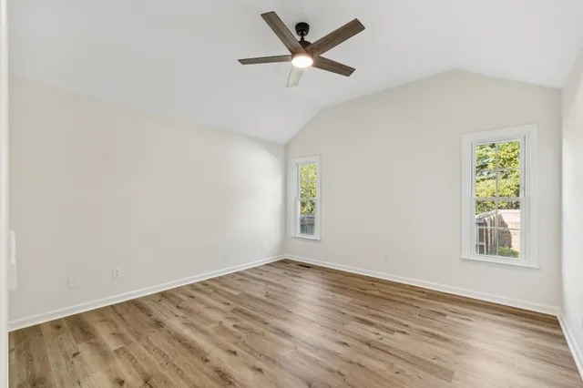 an empty room with wooden floor ceiling fan and windows