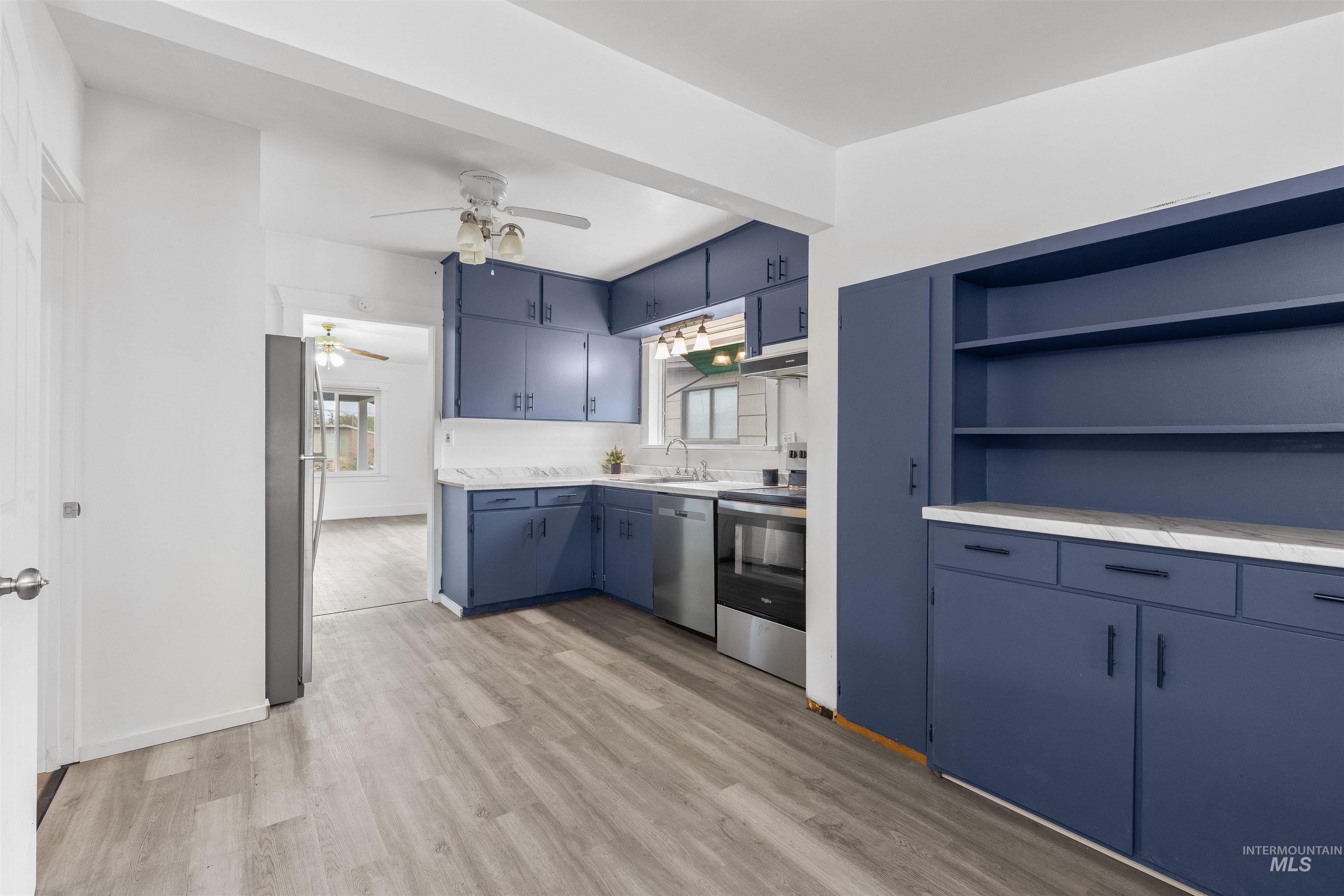716 7th Street Clarkston, WA 99403 - Photo 10 of 38 Kitchen with blue cabinets, light countertops, open shelves, light wood finished floors, and stainless steel appliances