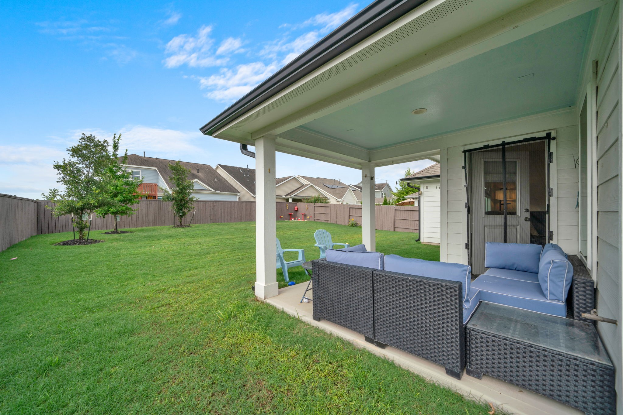 2503 Hagerman Road Conroe, TX 77384 - Photo 3 of 43 This photo showcases a spacious backyard with a covered patio area, featuring comfortable outdoor seating. The yard is well-maintained, fenced, and offers privacy with neighboring houses visible in the distance.