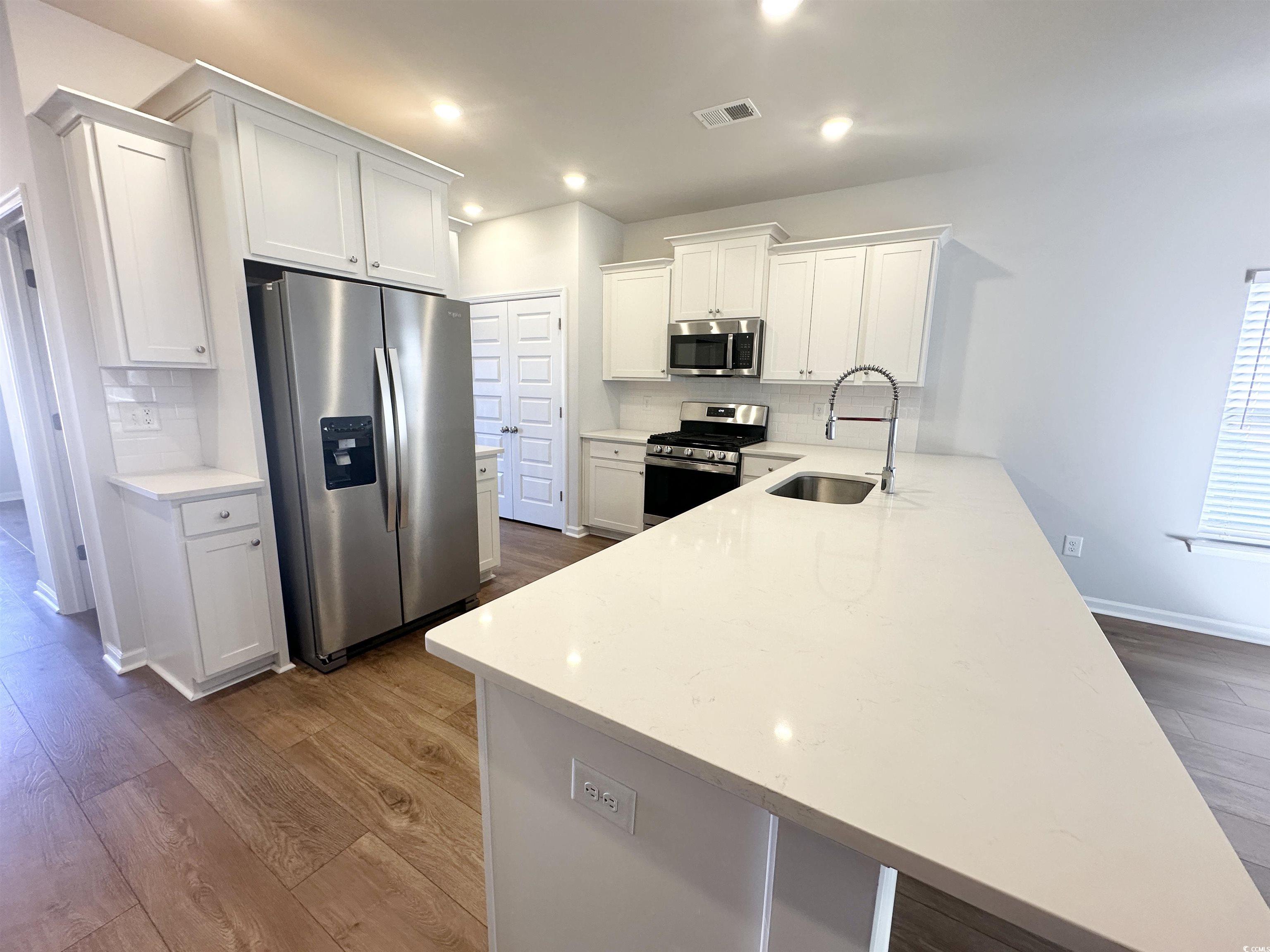 285 Augusta Grn Way Myrtle Beach, SC 29579 - Photo 6 of 28 Kitchen featuring stainless steel appliances, white cabinetry, decorative backsplash, light stone counters, and a peninsula