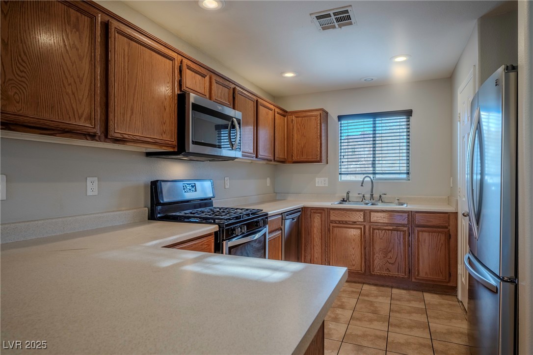5283 Broadlake Lane Las Vegas, NV 89122 - Photo 32 of 36 Kitchen with brown cabinets, stainless steel appliances, light countertops, light tile patterned flooring, and recessed lighting